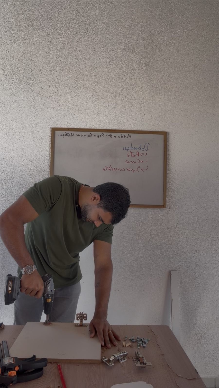 Instrutor furando uma peça com a furadeira, com dobradiças sobre a bancada